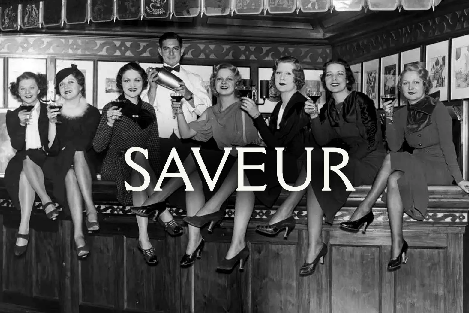 Black and white photo of women in dresses and high heels with legs crossed sitting on a bar counter, with a bartender in the background holding a cocktail shaker, drinking glasses in hand, with the word 'SAVOUR' written across the center.