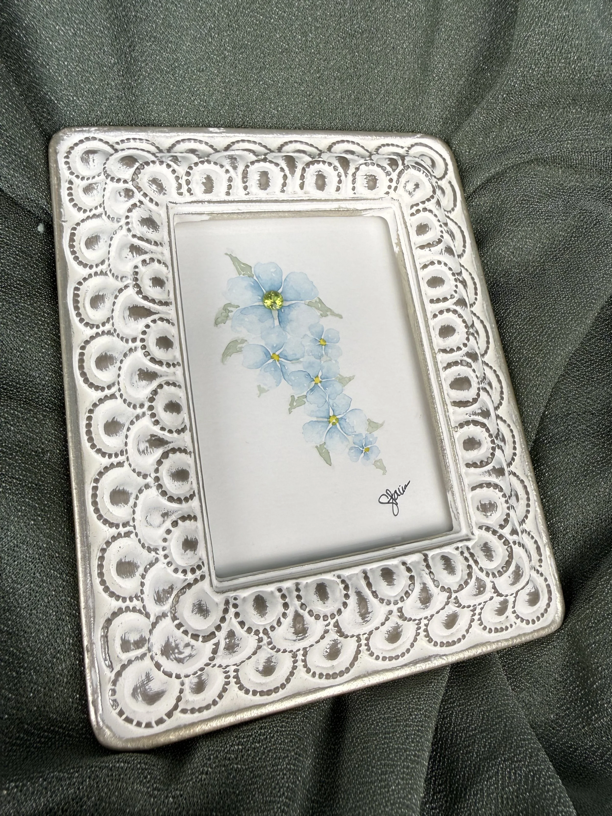 Blue Cascade watercolor painting of cascading blue flowers with a natural peridot gemstone center in a white and silver frame by Stacia Shane