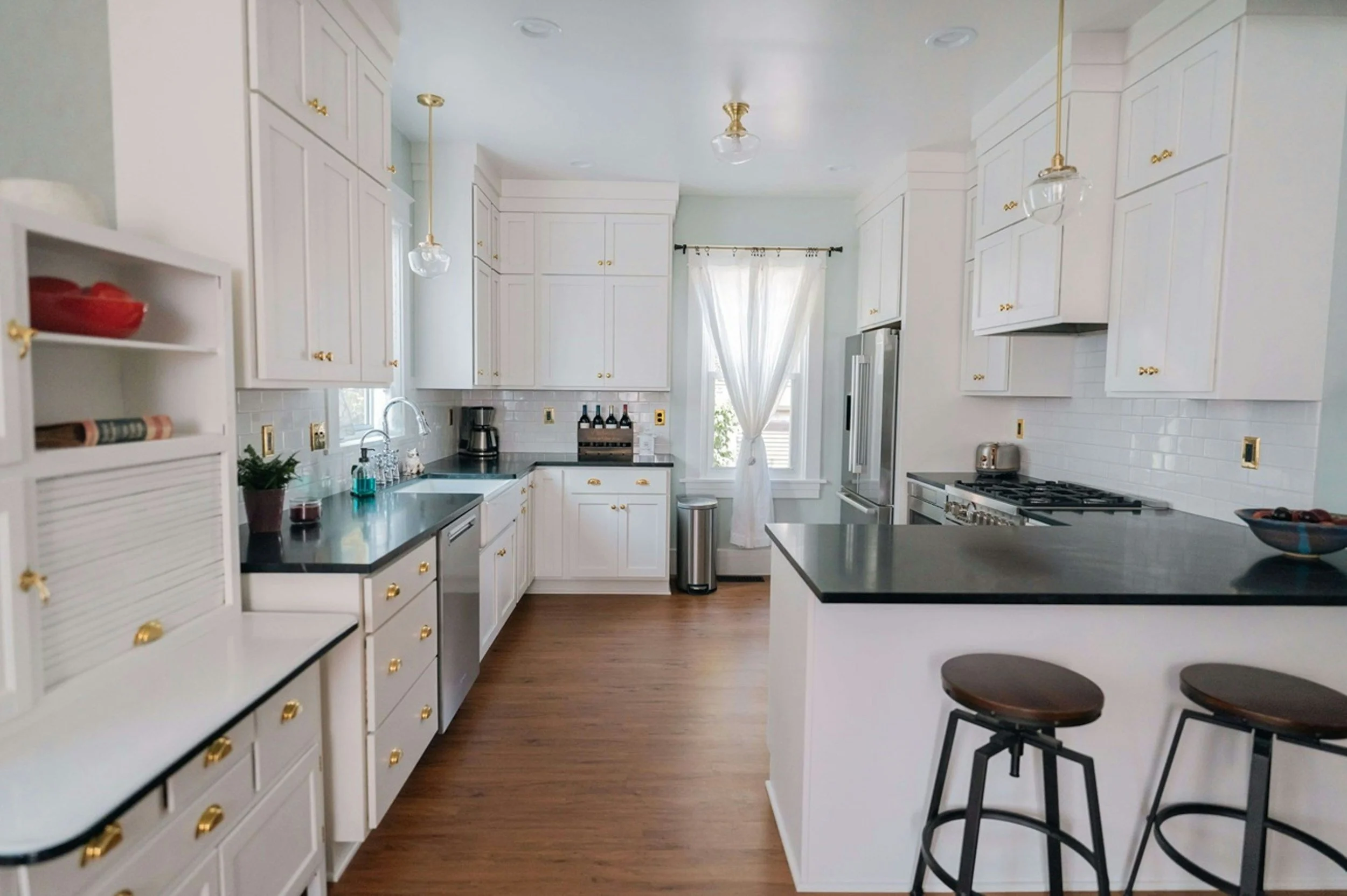 Bright kitchen with white cabinets, black countertops, hardwood flooring, and two hanging pendant lights.