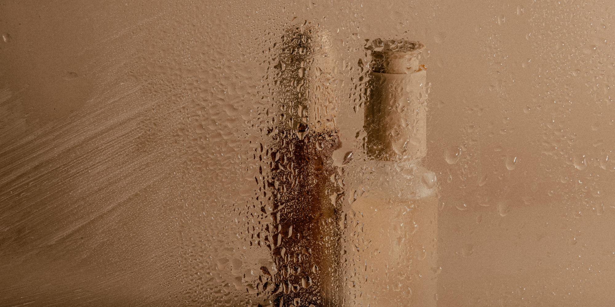 A private bathroom mirror fogged up with condensation, with a partially visible skin care product.