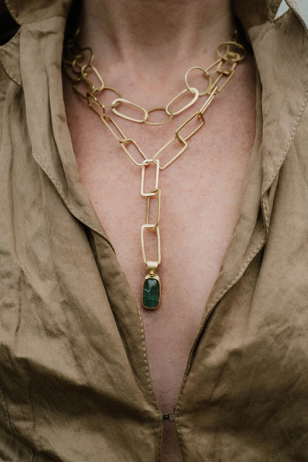 Close-up of a person wearing layered gold chain necklaces and a beige shirt with a partially unzipped collar.