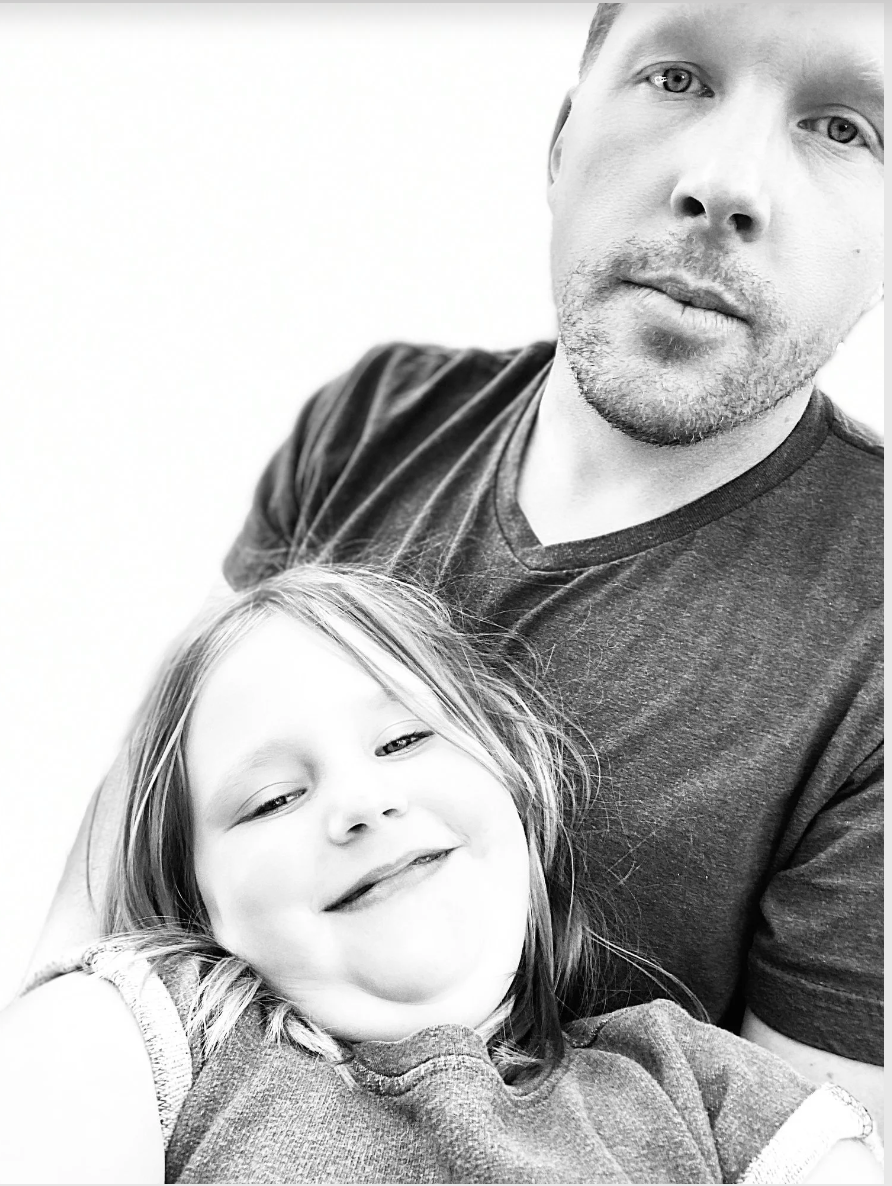 A black and white photo of a man and a young girl, smiling and close together, with the man slightly off-center.