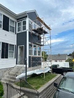 Scaffolding set up outside a multi-story residential building with white and blue siding, indicating ongoing exterior renovations.