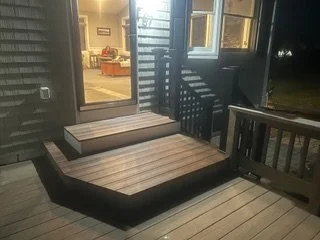 Wooden outdoor deck with a shaded porch area, showing part of a house interior visible through glass doors.