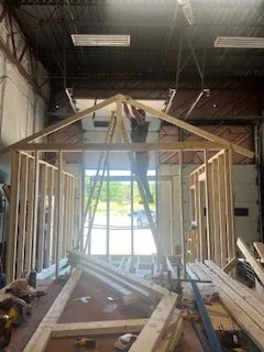 Person working on building a wooden frame structure inside a workshop.