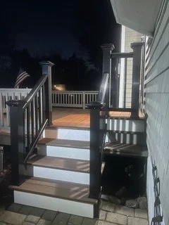 Nighttime view of a small outdoor deck with wooden stairs and railing attached to a house.