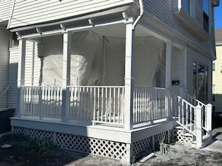Porch with white railing and steps leading up to it, enclosed with transparent screens or plastic.