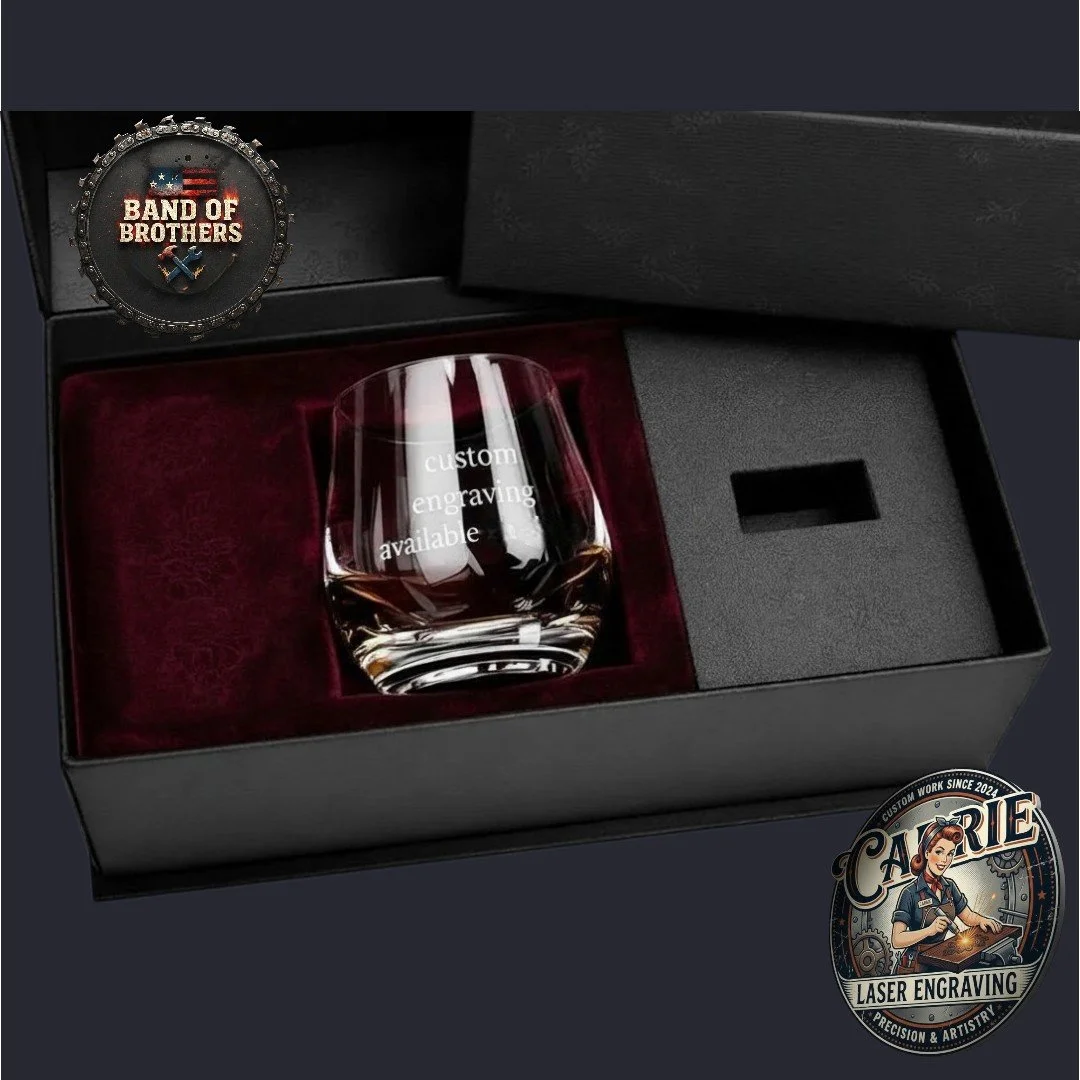A glass whiskey decanter with an engraved message that reads 'custom engraving available' inside a black gift box with a red velvet lining, and branded patches from 'Band of Brothers' and 'Catie Laser Engraving'.