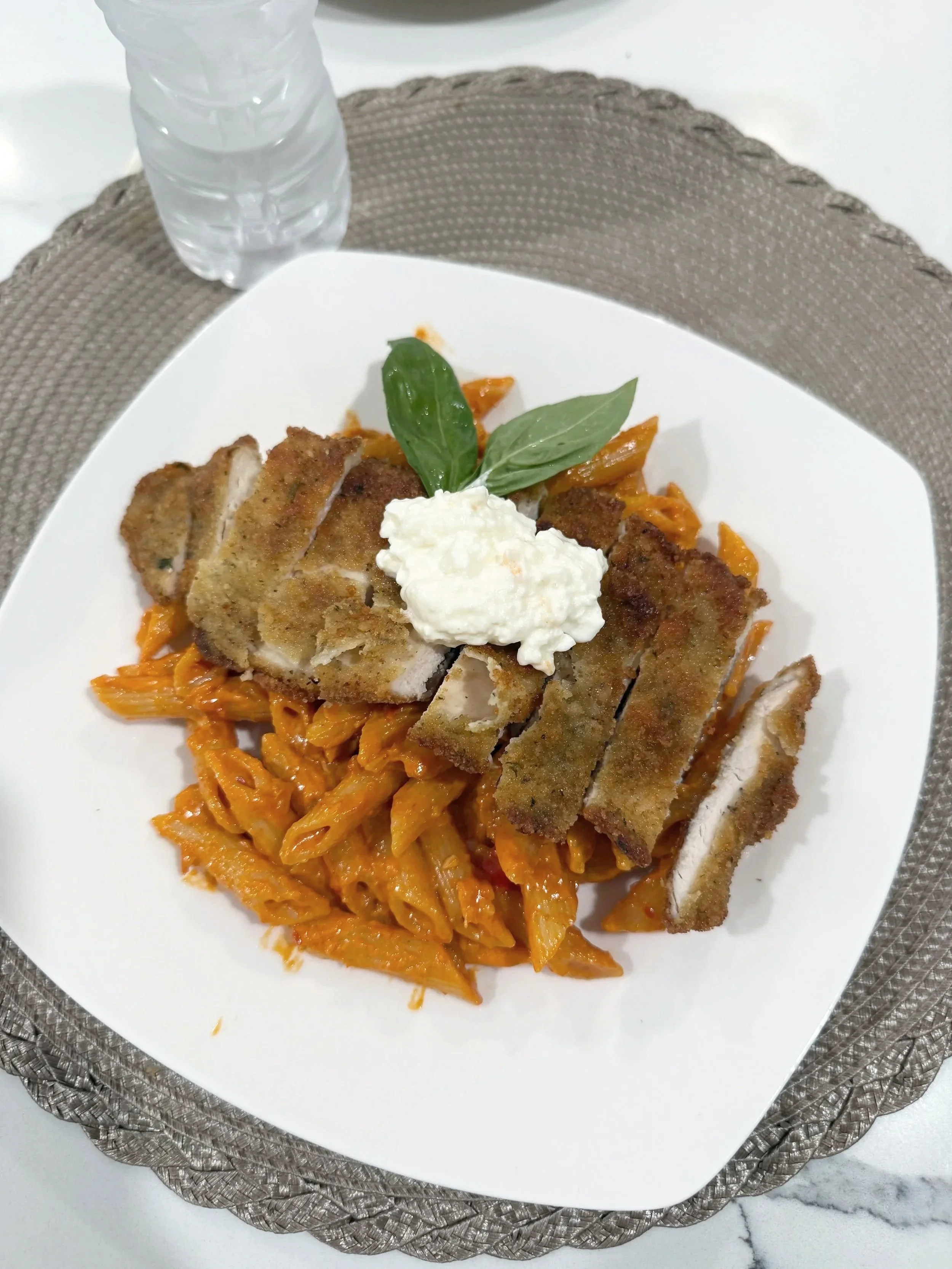 Plate of breaded meat cutlets with a dollop of white sauce, garnished with basil leaves, served over a bed of cooked shredded vegetables, possibly carrots or sweet potatoes, on a white plate with a decorative silver placemat underneath.