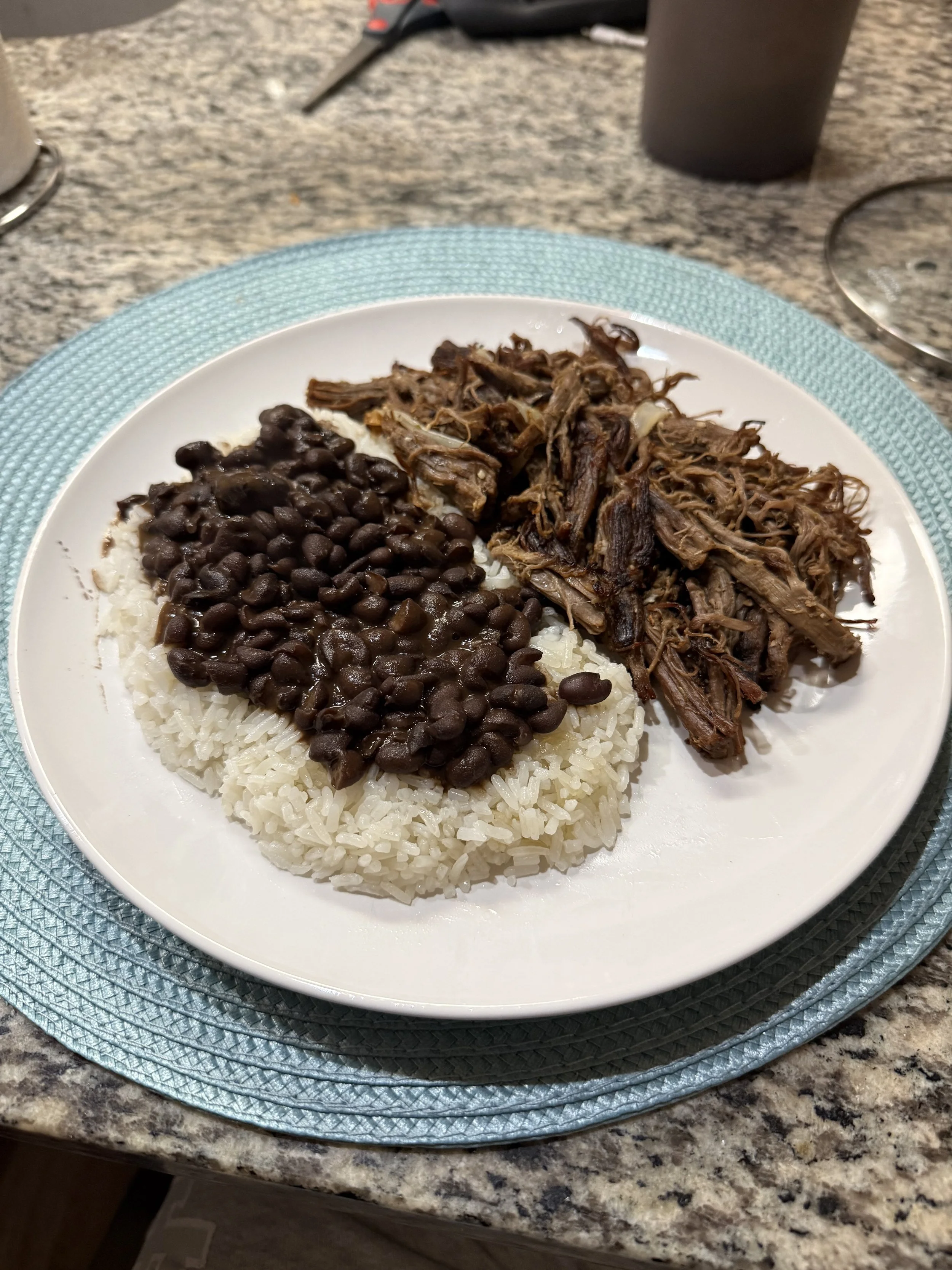 Plate with black beans, shredded beef, and white rice on a blue placemat on a granite countertop.