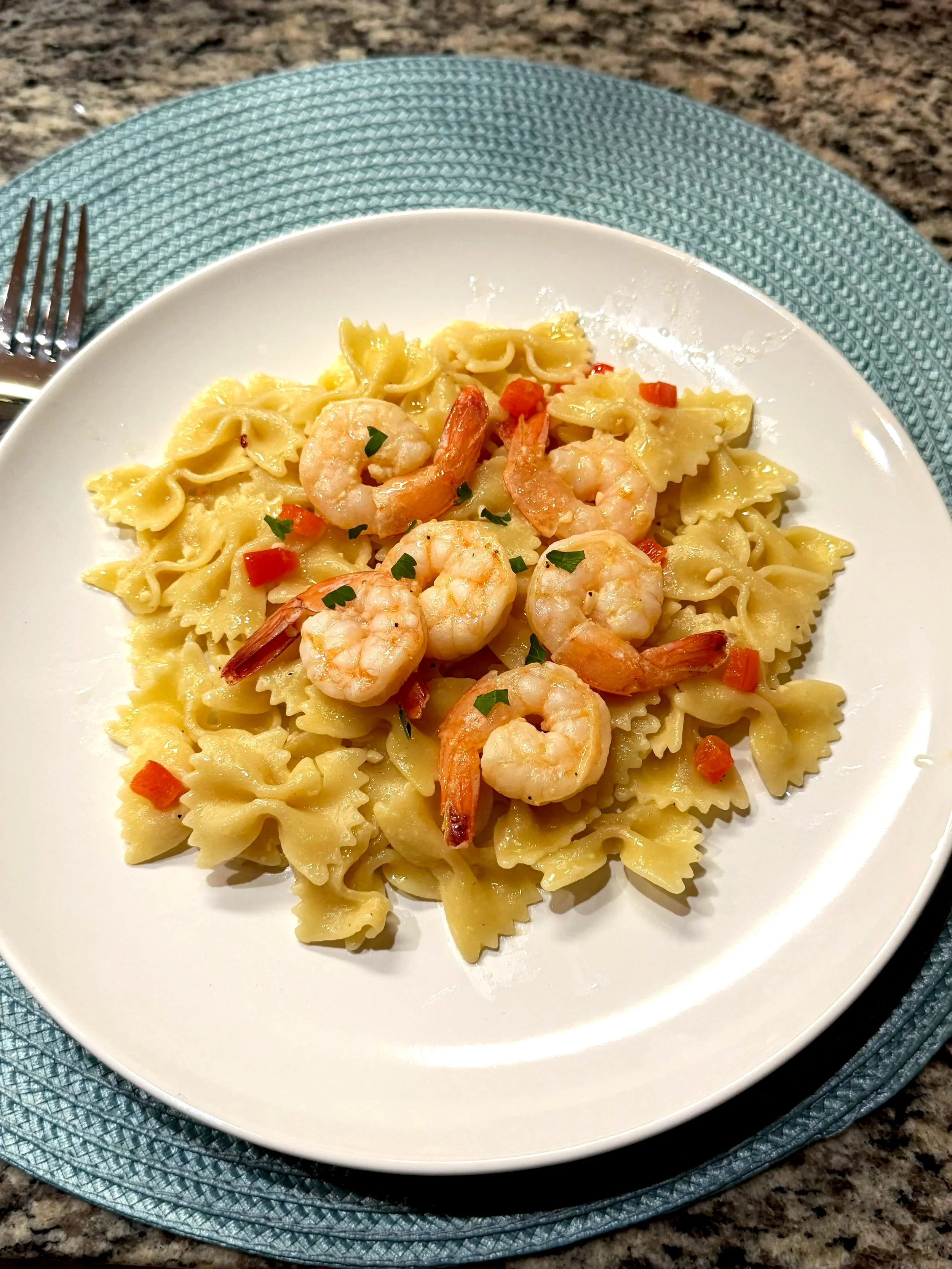 Plate of cooked bowtie pasta with shrimp and small pieces of red and green peppers, garnished with chopped herbs.