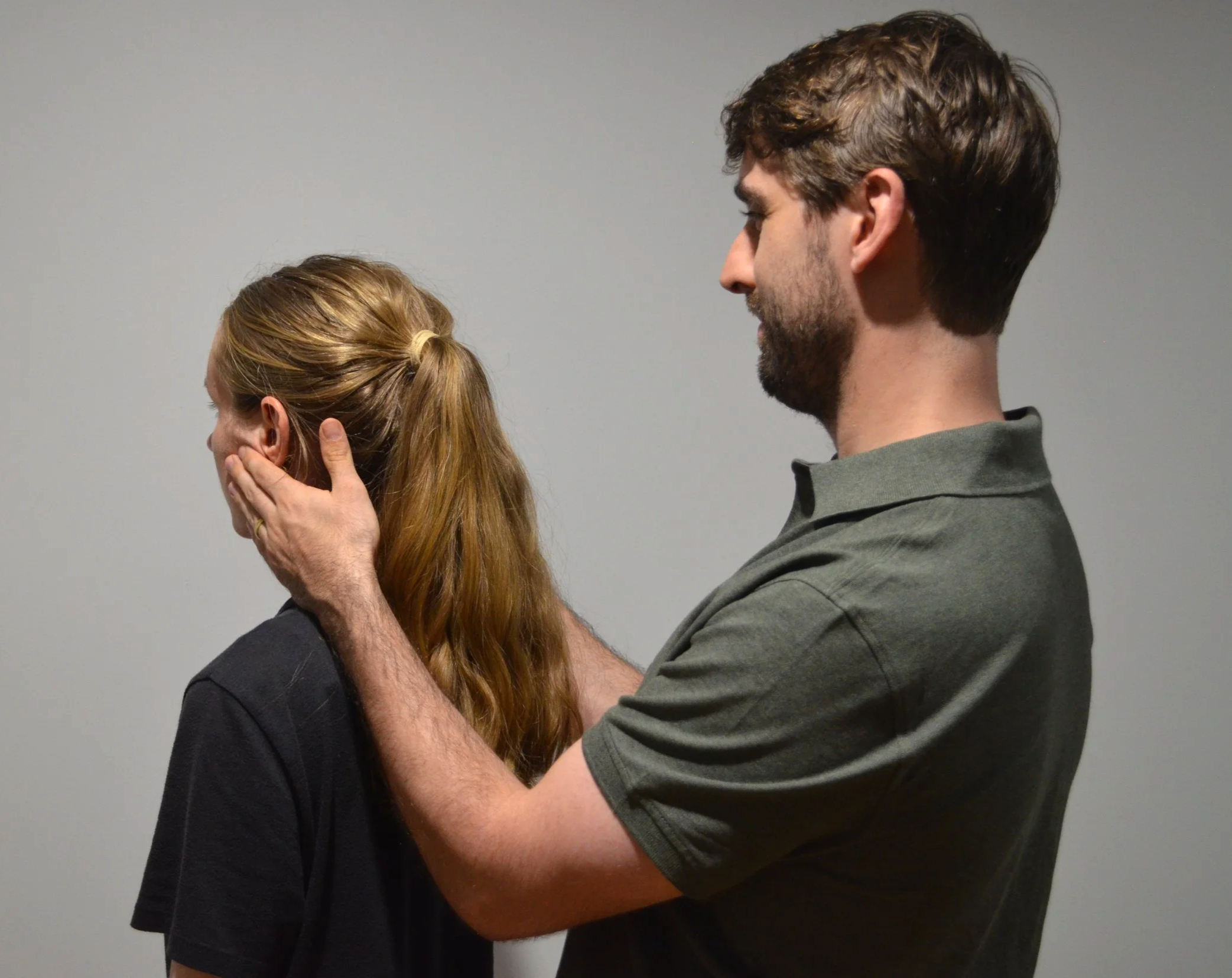 A male physiotherapist treats a female patient facing away from him for TMJ disorder.