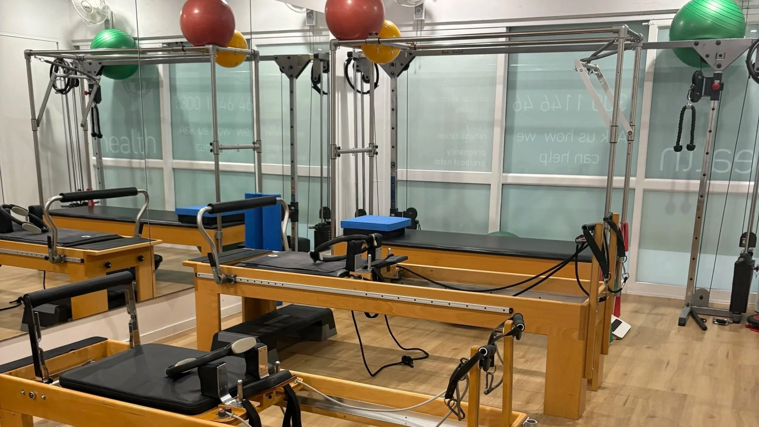 Physiotherapy and rehabilitation gym with wooden treatment tables, suspension straps, exercise balls, and mirrors.
