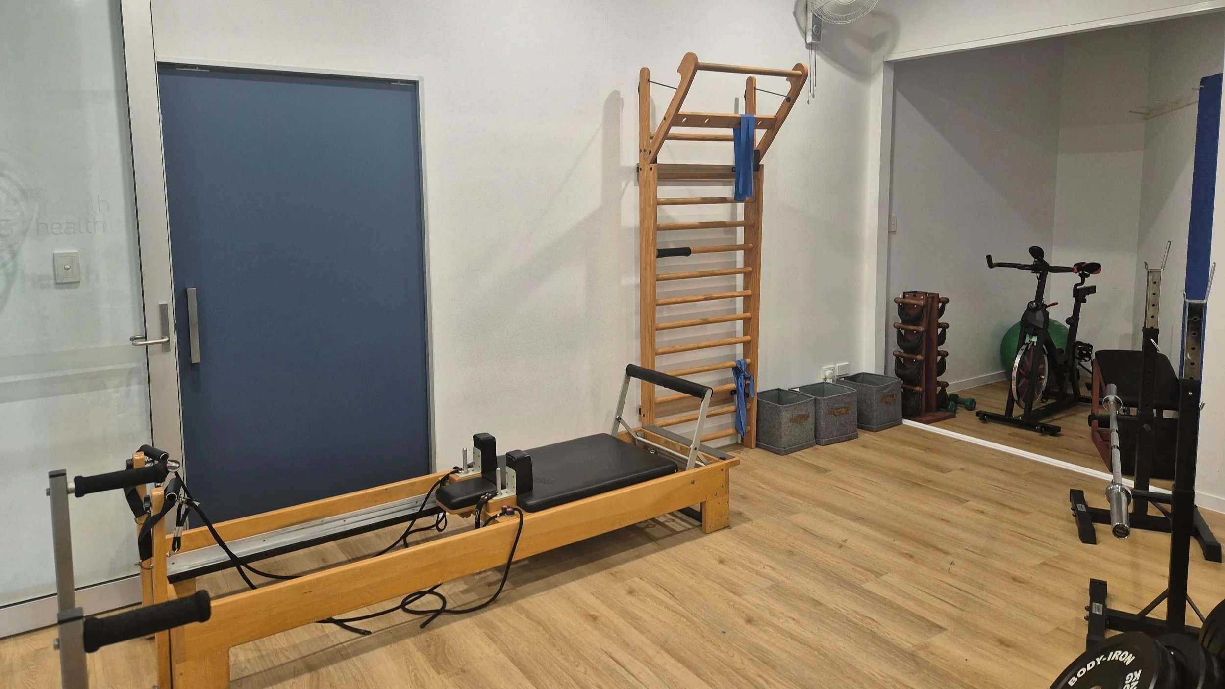 A physiotherapy gym with wooden workout equipment, treadmill, stationary bike, and various exercise accessories on hardwood floors.
