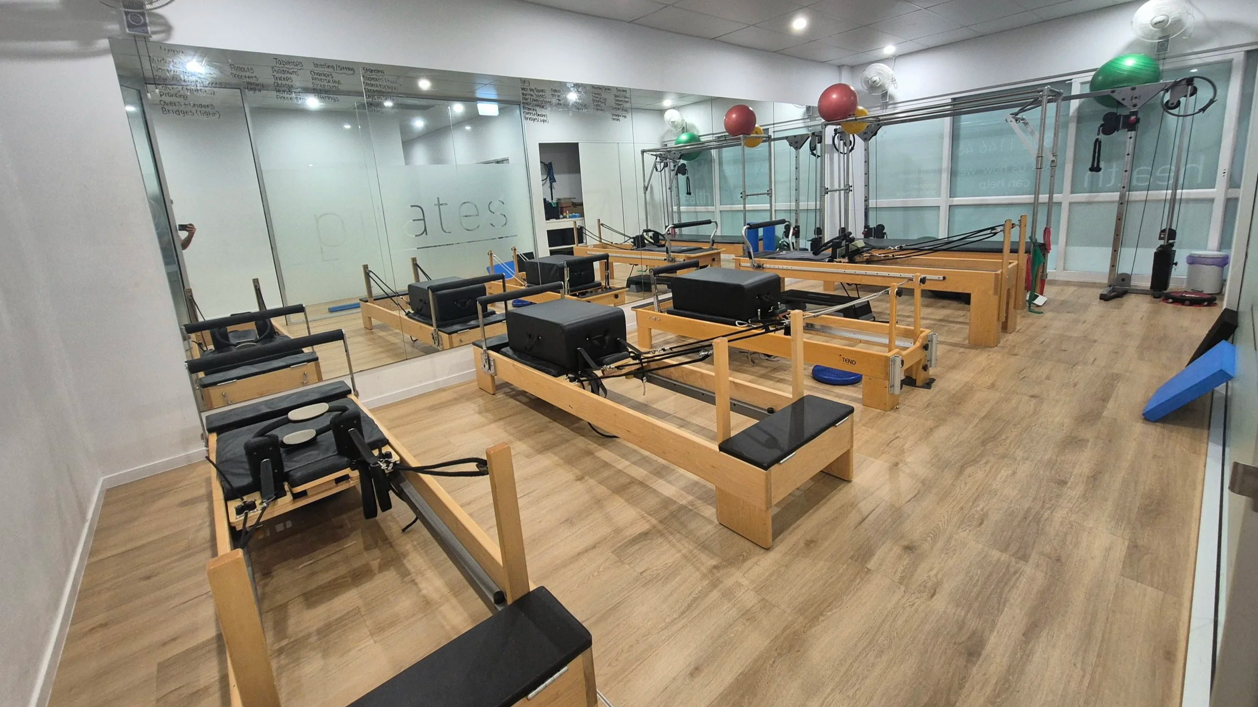 Physiotherapy reformer pilates studio with wooden reformer machines, exercise balls, and a large mirror on the wall.