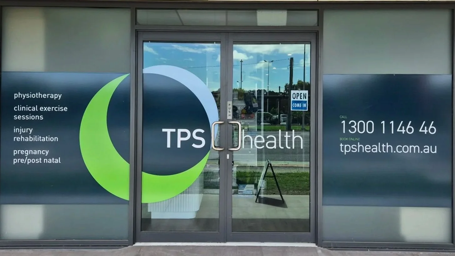 TPS Bayside Capalaba front facade with large dark gray and green logo, contact number, website, and list of health services including physiotherapy, clinical exercise, injury rehabilitation, pregnancy, and pre/post natal care.
