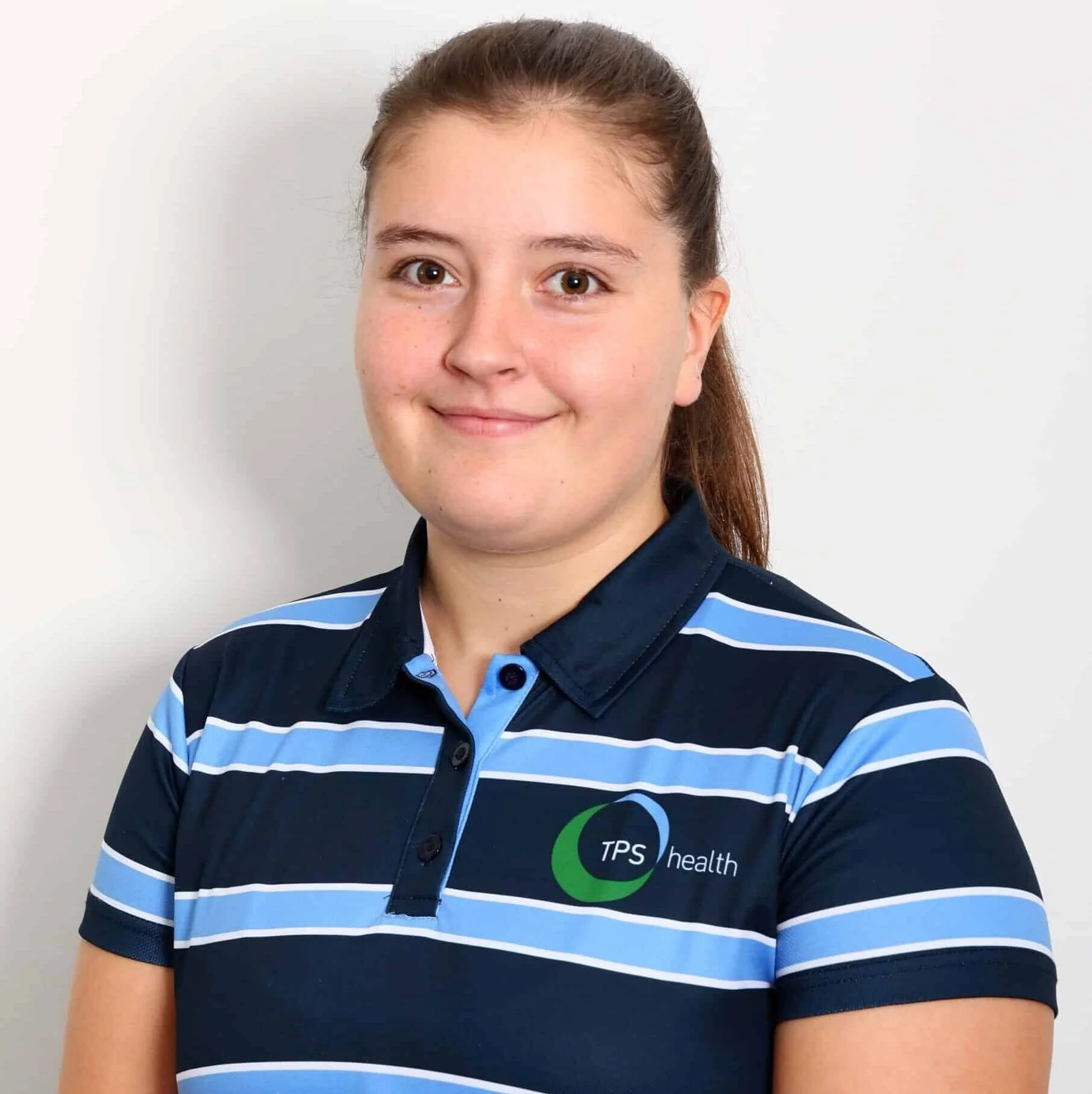 Smiling female physiotherapist, wearing a navy blue and light blue striped polo shirt with a TPS Bayside Capalaba and Victoria Point logo, standing against a plain white background.