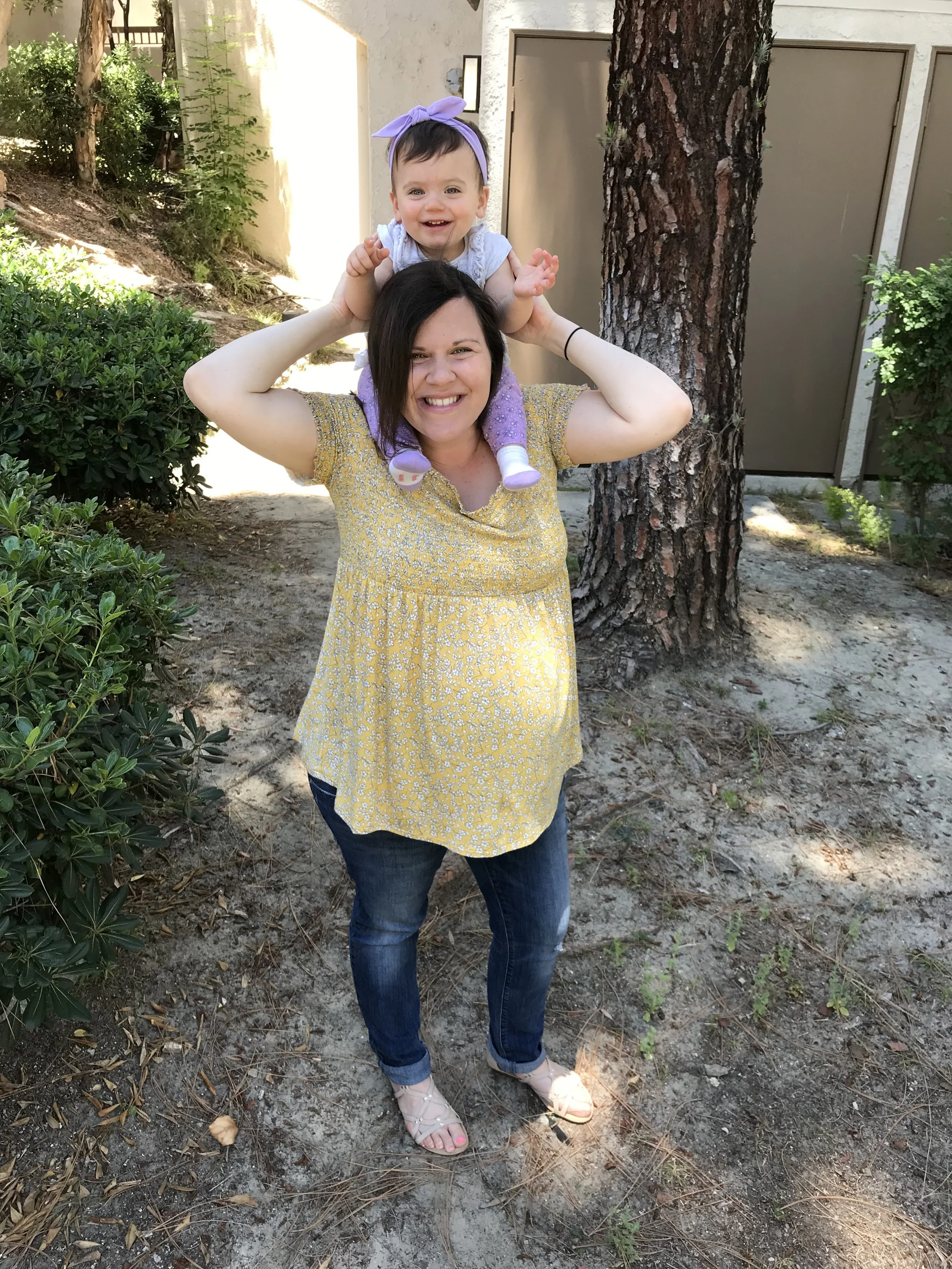 Pregnant momma with twins giving her one year old daughter a piggy back ride.