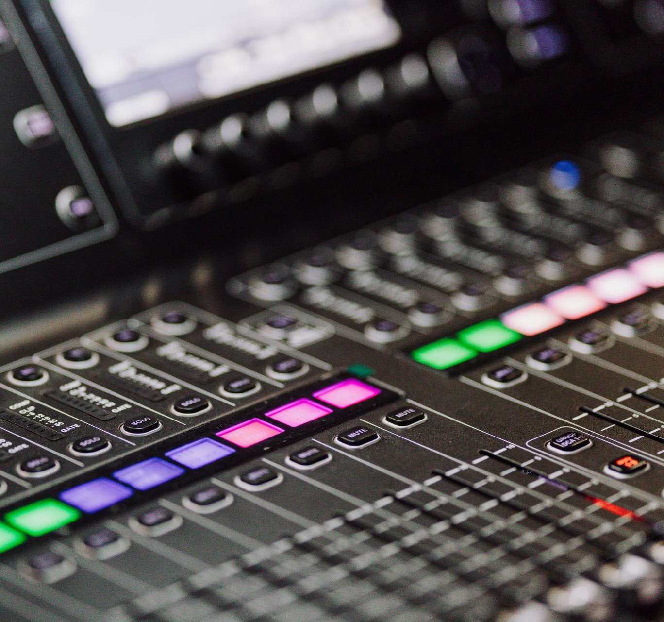 Close-up of a professional audio mixing console with colorful LED buttons and sliders.