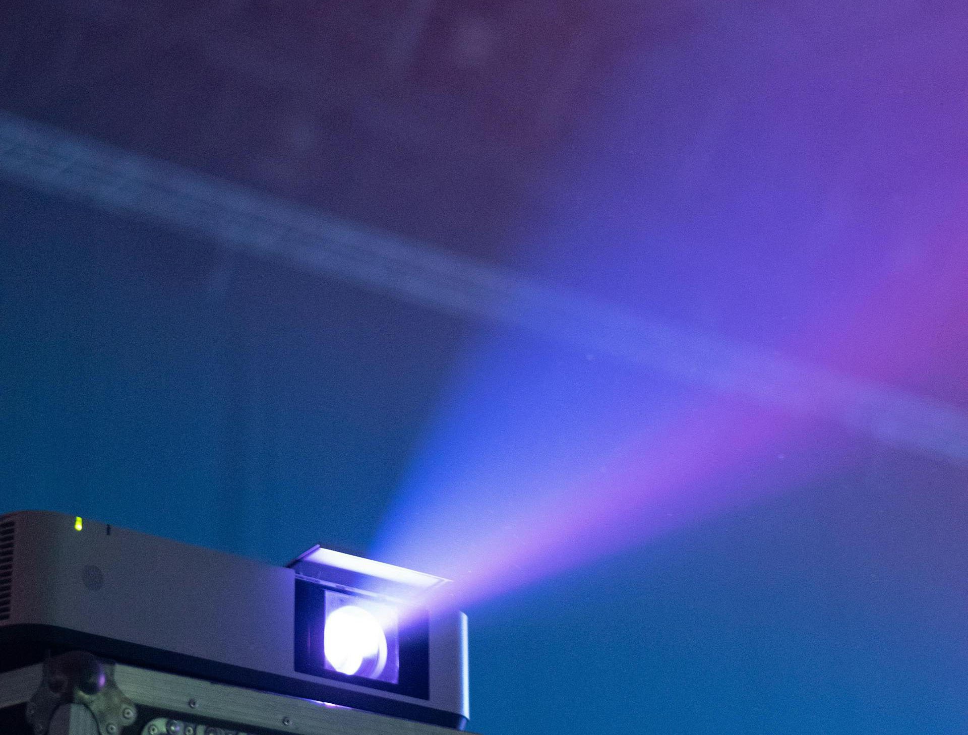 Part of a computer with a glowing purple light and a background with blended blue, purple, and pink lighting.