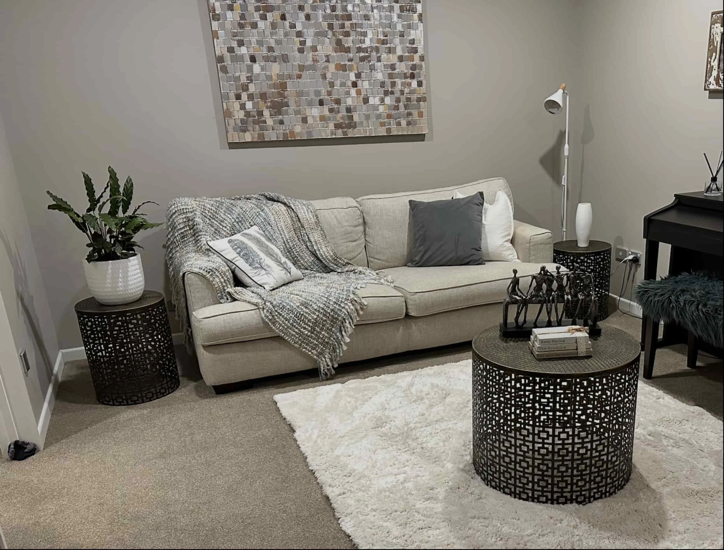 Neutral-toned living room ideal for neuro rehab, with a beige sofa, textured throw, round tables, plant, wall art, and fluffy rug..