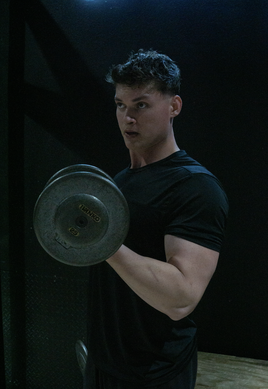 Young man in black t-shirt lifting a dumbbell in a gym.