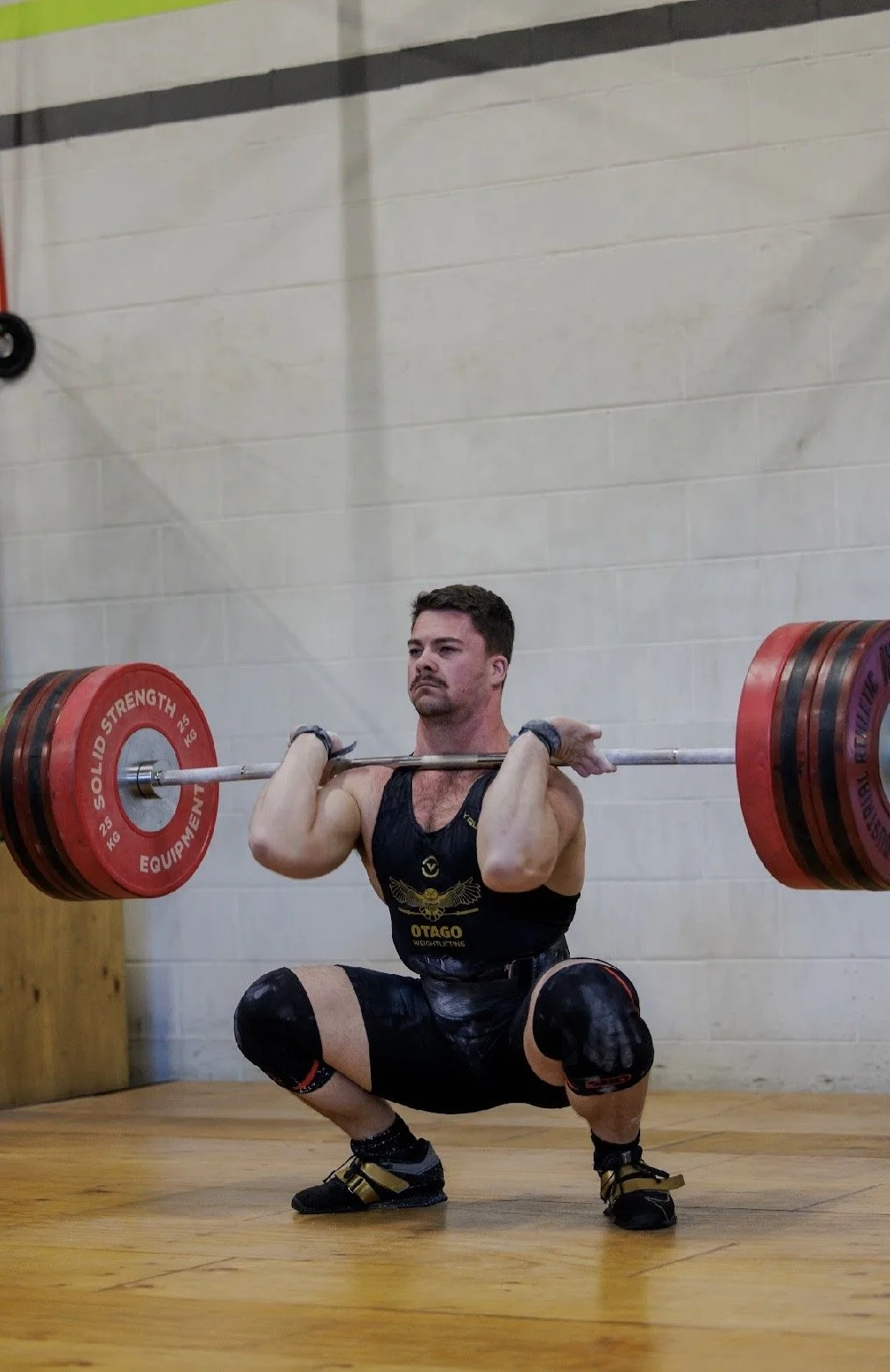 A man in athletic gear performing a squat while lifting a barbell with weight plates in a gym.