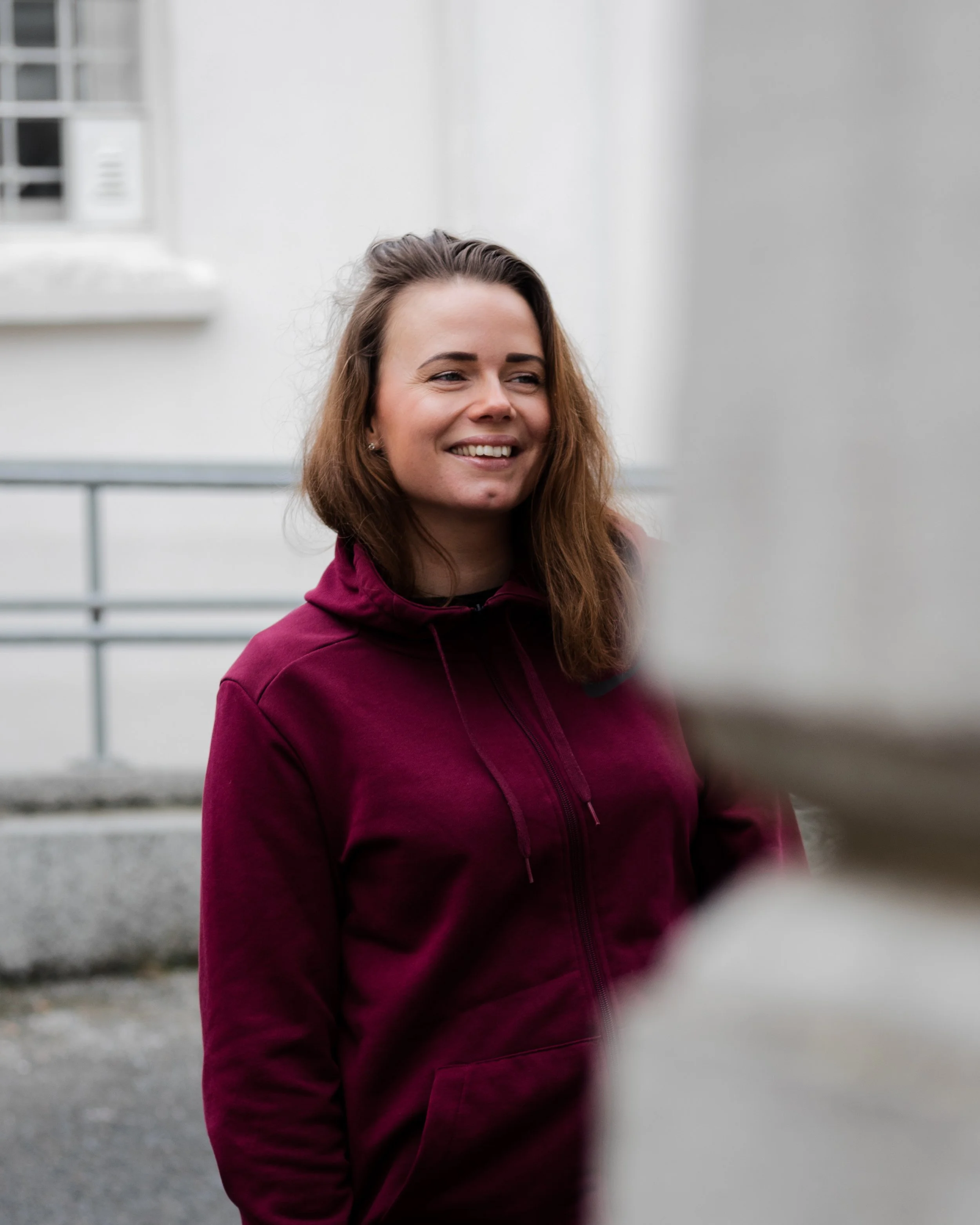 Kvinne med skulderlangt hår smiler utendørs – kreativ gründer i avslappet setting.