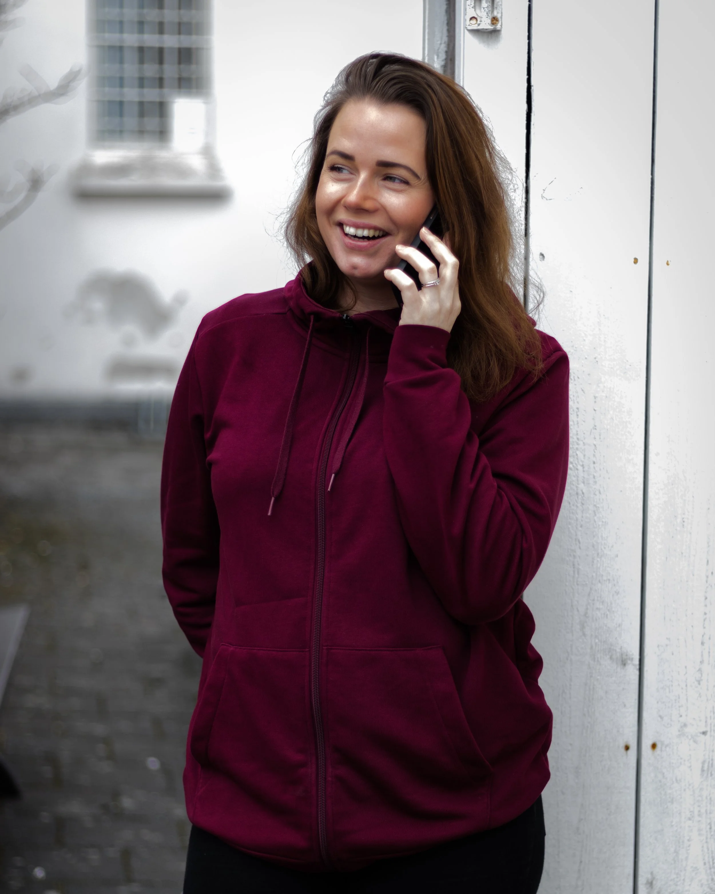 Kvinne i burgunder hettegenser snakker i telefon og smiler – gründer som jobber med egen business.