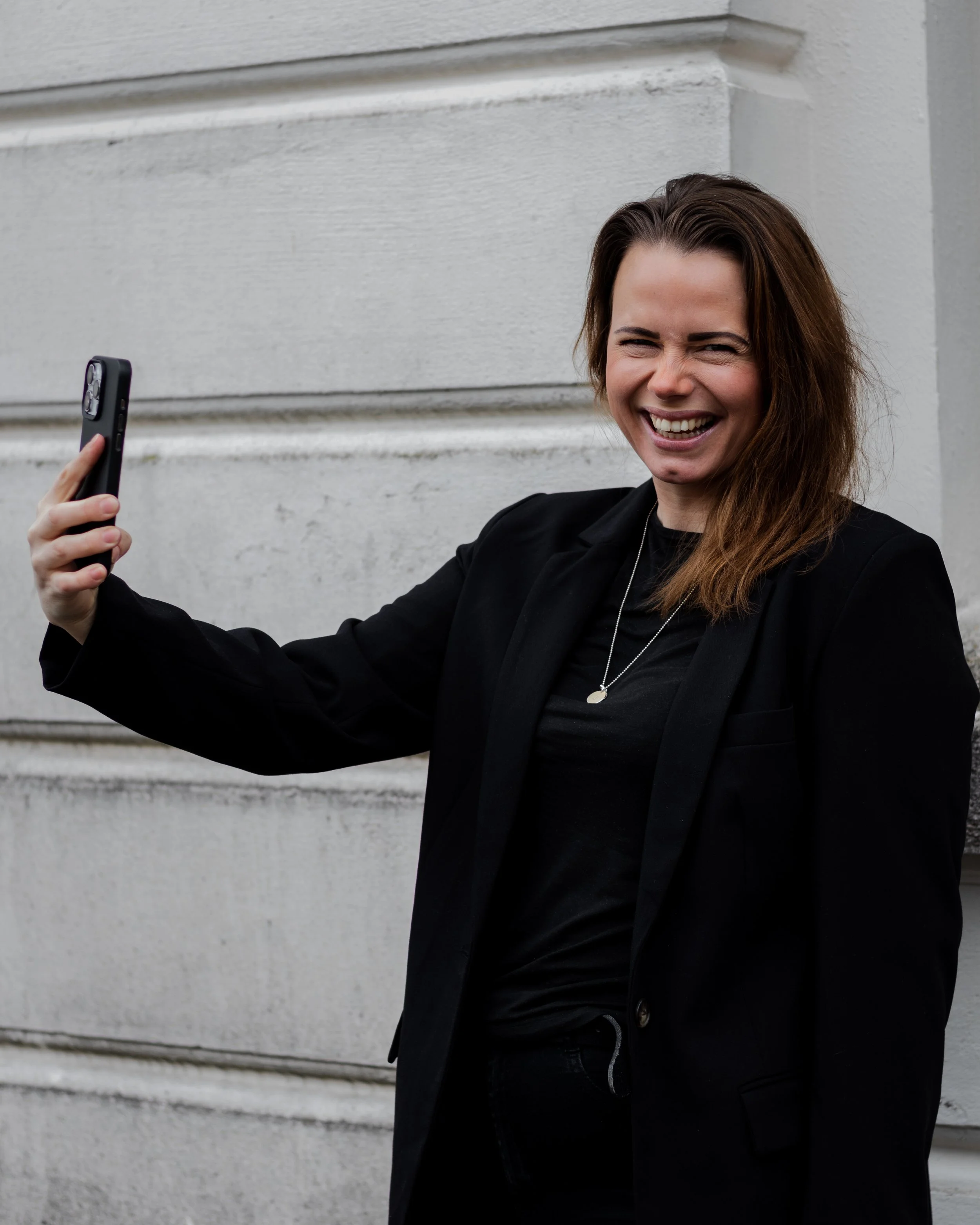 Kvinne i svart blazer tar selfie og smiler ute – personlig merkevare og synlighet på nett.