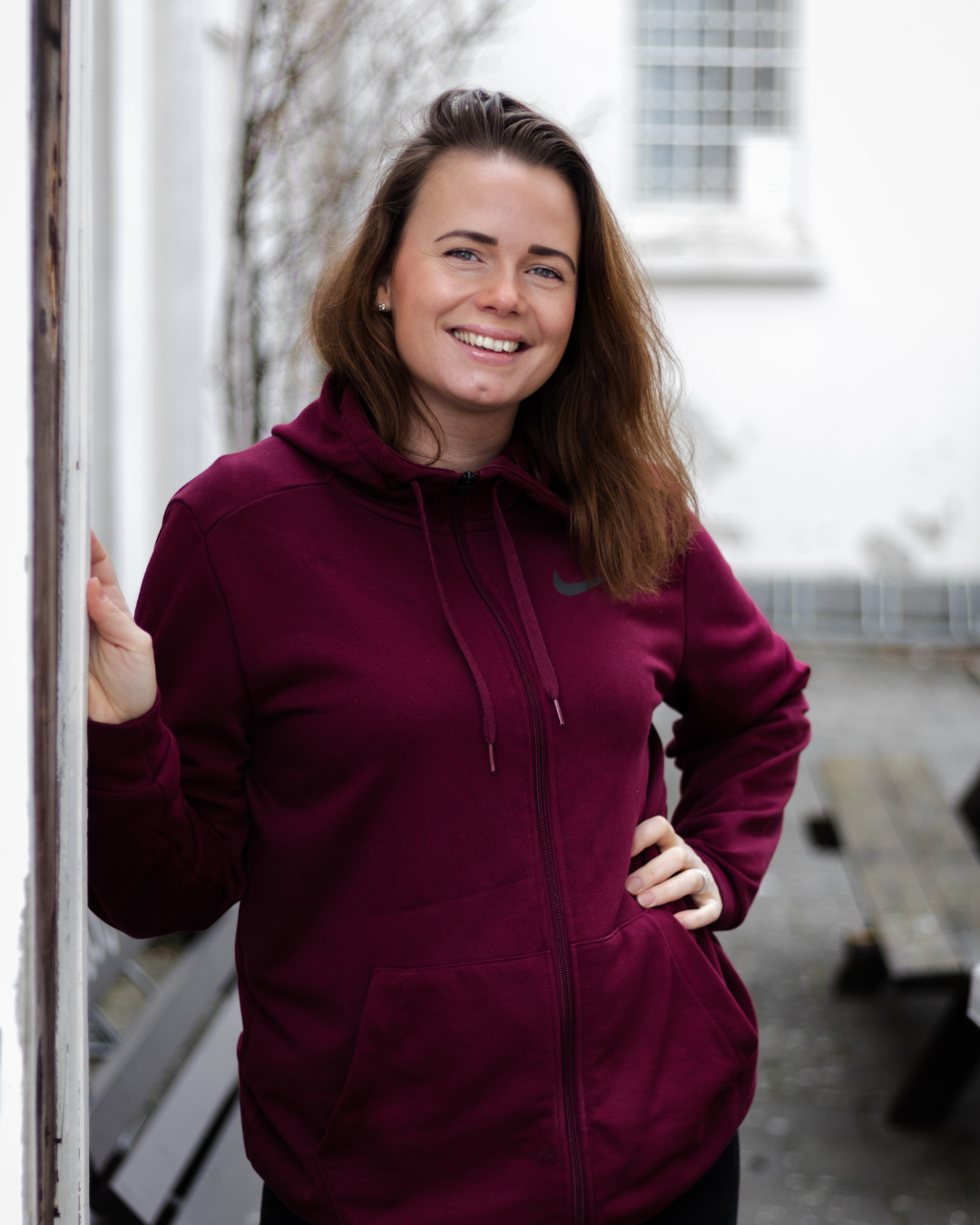 Ung kvinne i hettegenser smiler utendørs – jobber med egen business og digitale løsninger.