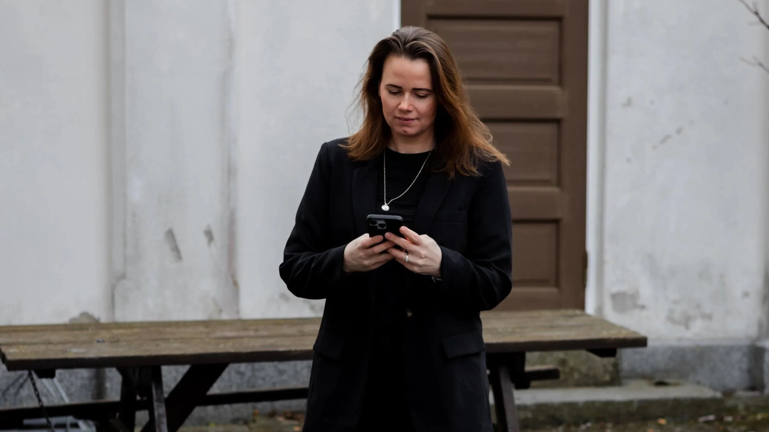 Kvinne i svart blazer står ute og ser på mobilen – jobber med digitale løsninger og nettsider.