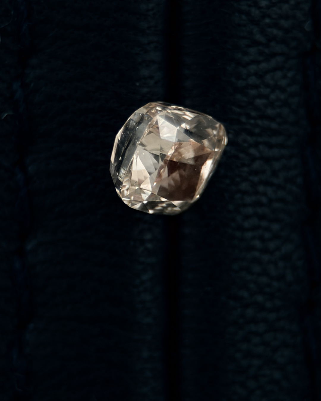 Close-up of a large, faceted diamond resting on a dark, textured fabric background.