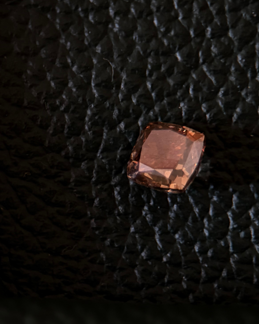 A close-up of a fancy colored diamond, yellow-orange resting on a brown leather surface.