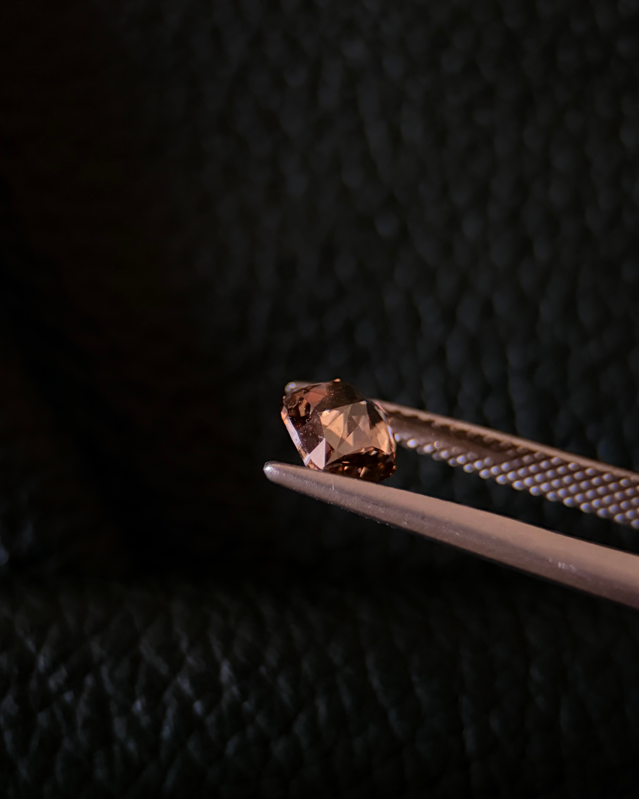 A small gemstone held by tweezers against a dark background.