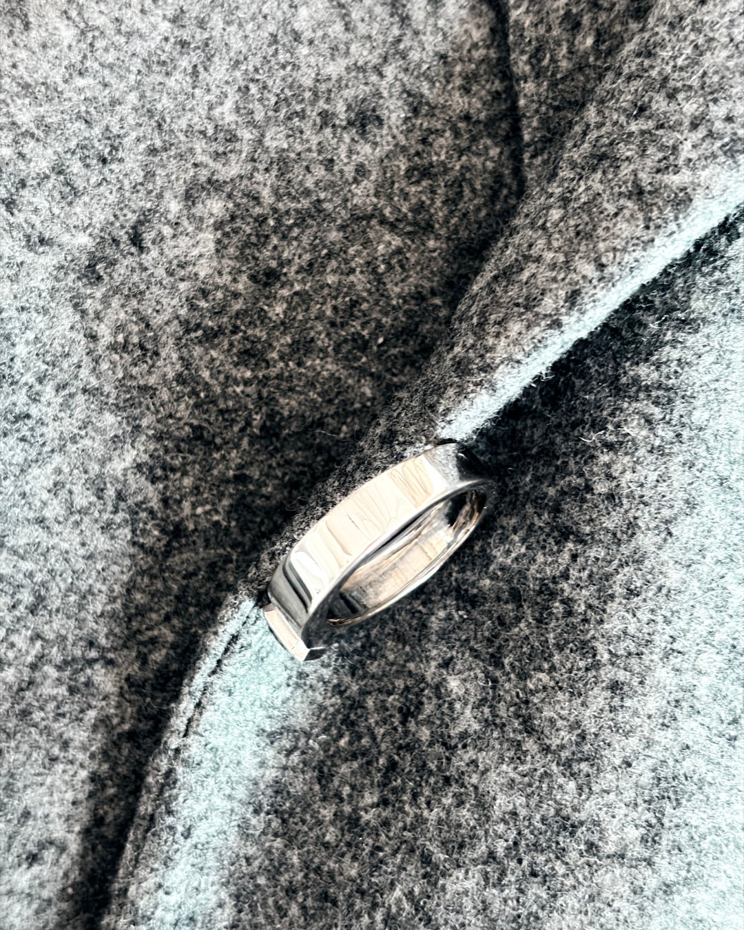 A 18k white gold ring with a fancy colored diamond is placed on a gray fabric surface.