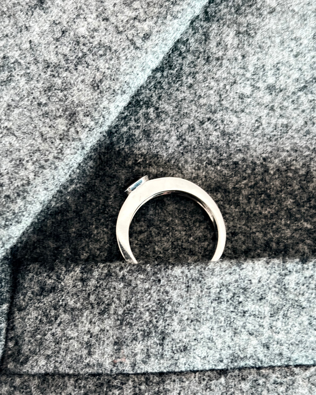 A 18k white gold ring with a fancy colored diamond is placed on a gray fabric surface.