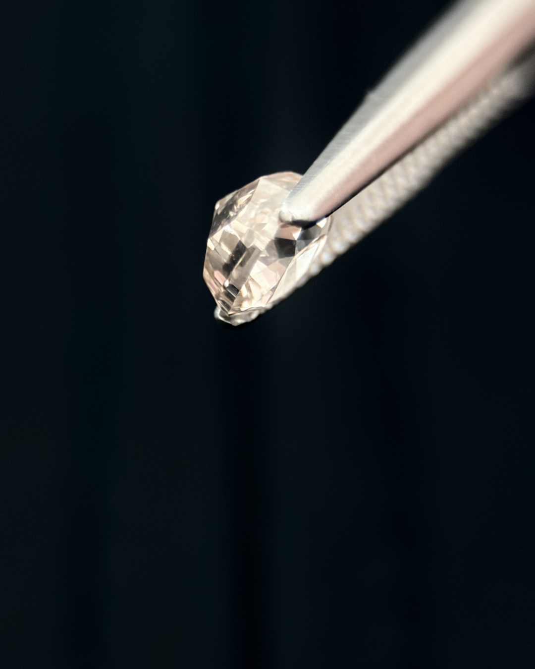 A close-up image of a heart-shaped diamond held with tweezers against a black background.