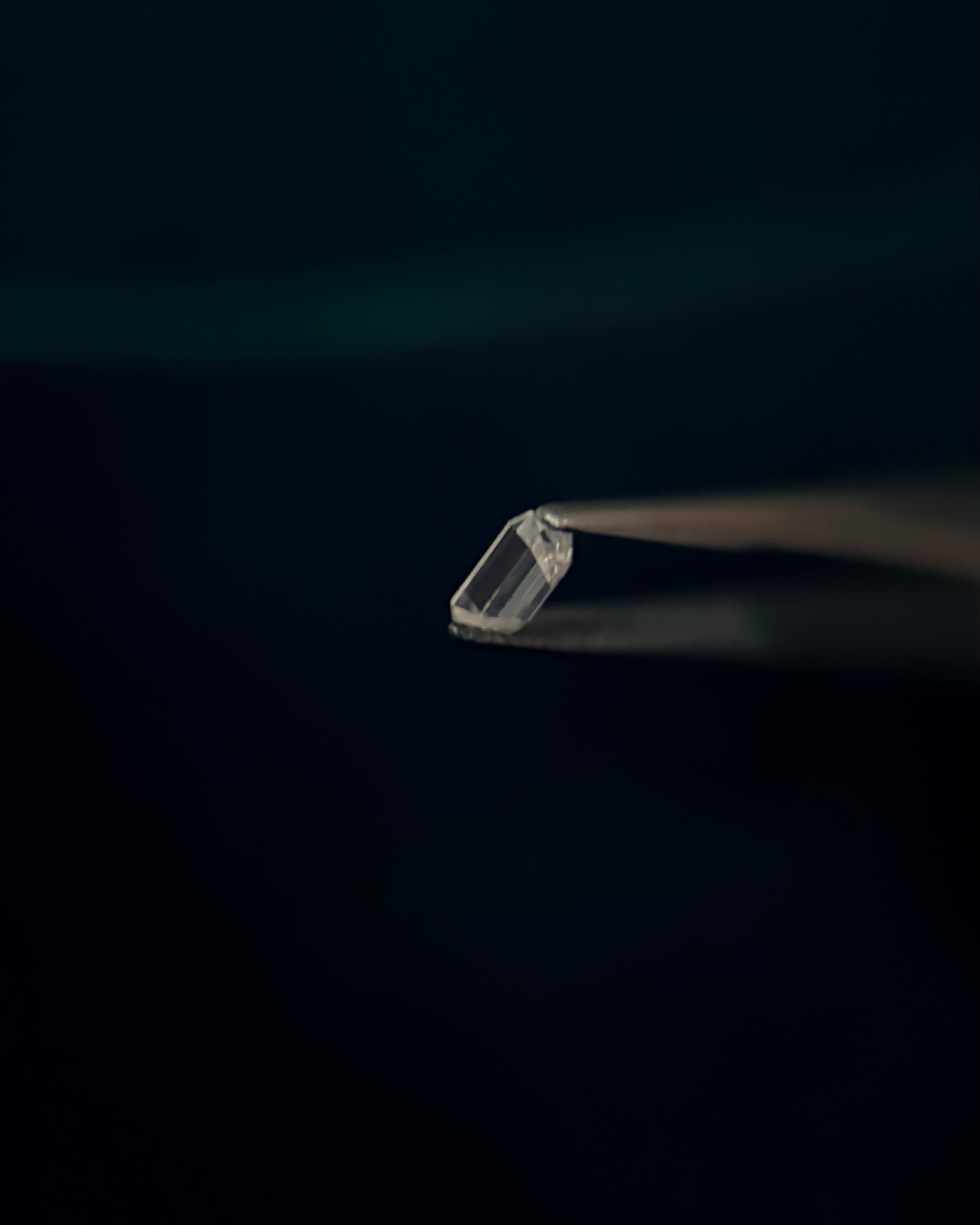 Close-up of a single, colorless diamond held with tweezers against a dark background.