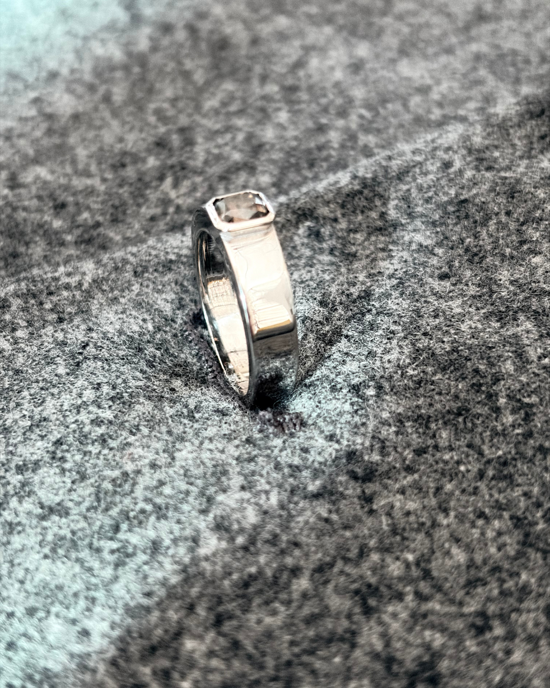 A 18k white gold ring with a fancy colored diamond is placed on a gray fabric surface.