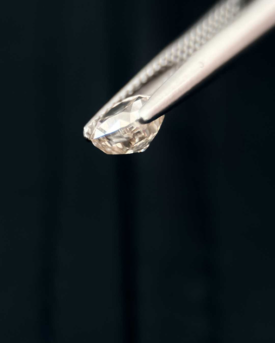 Close-up of a diamond held by tweezers against a dark background.