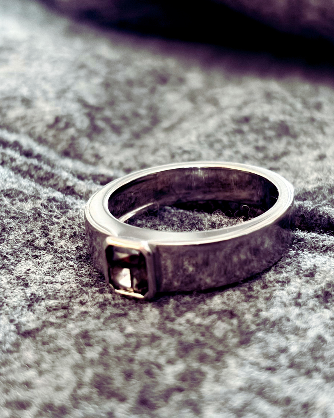 A 18k white gold ring with a fancy colored diamond is placed on a gray fabric surface.