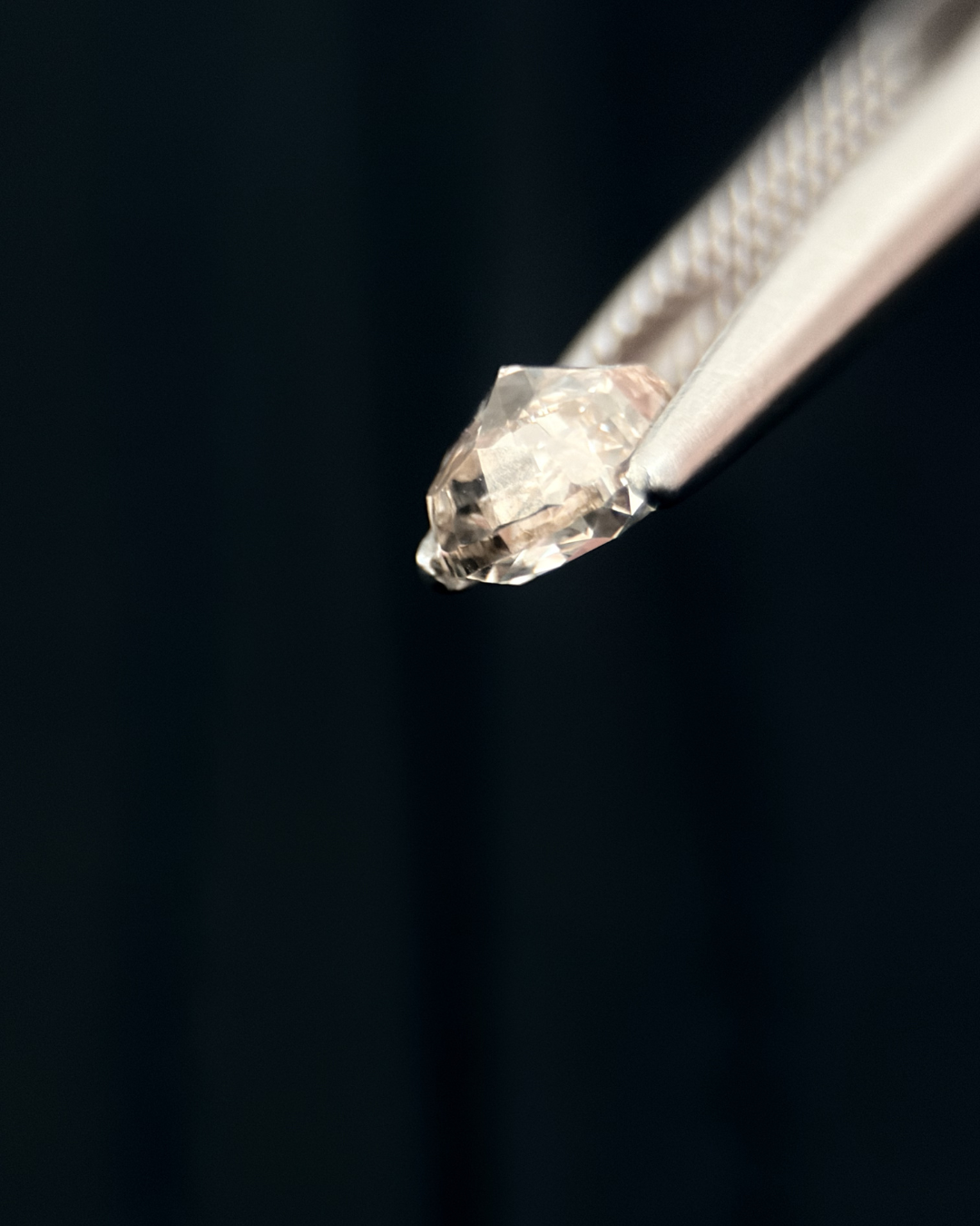 Close-up of a diamond held with tweezers against a dark background.