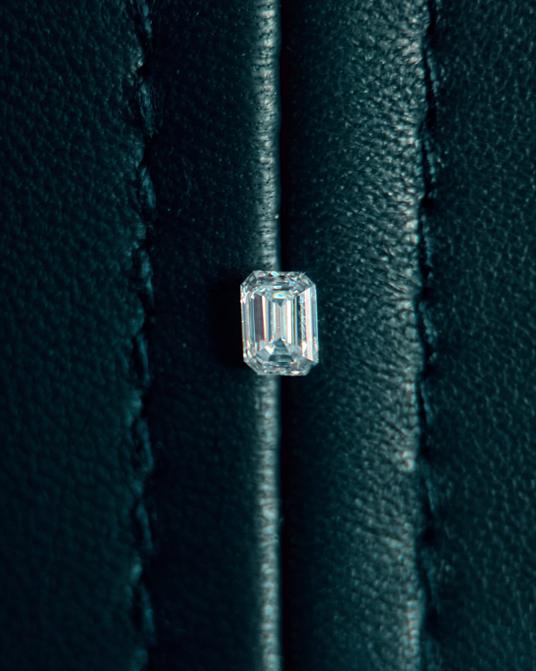 Close-up of a single, large, emerald-cut diamond on black textured leather surface.