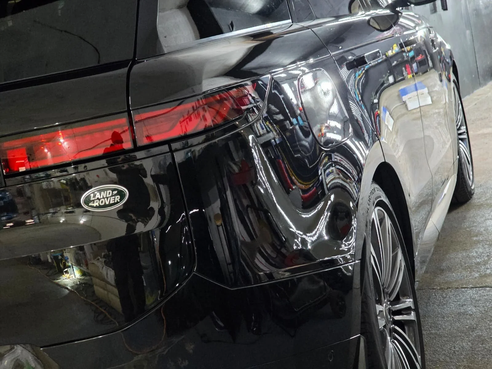 Black Land Rover vehicle parked indoors, with visible reflection of surroundings on its shiny surface, rear taillight, and wheel.