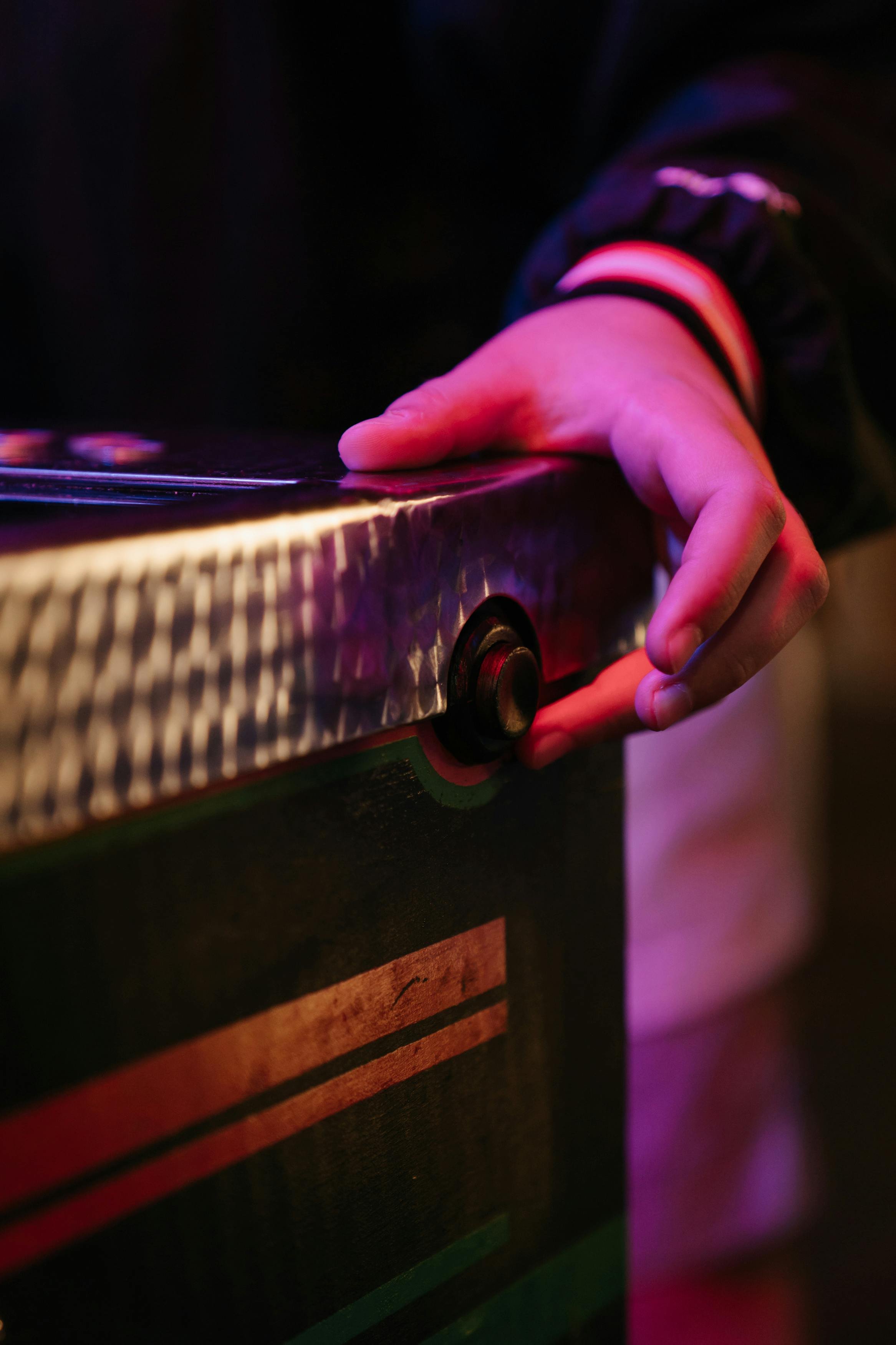 Close-up of a person’s hand turning a knob on a vintage arcade game machine, illuminated with colorful lights.