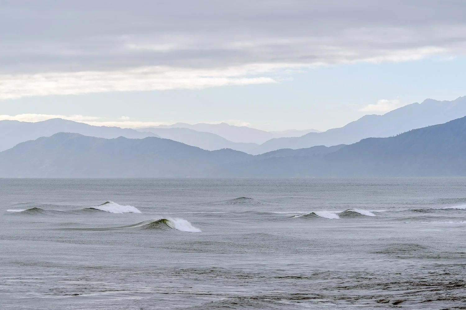 Rolling waves with layered mountain ranges on the West Coast.