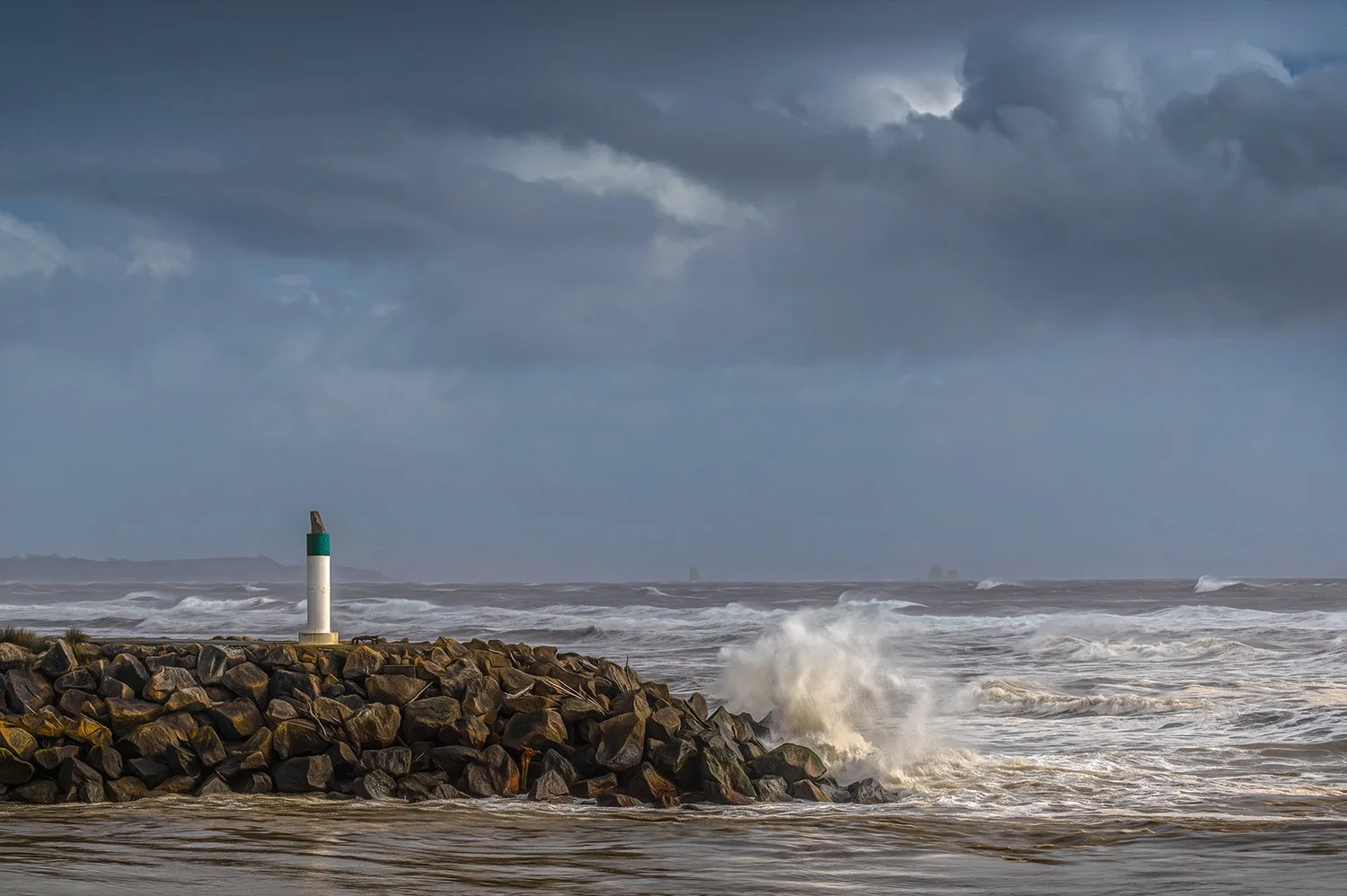 Harbour entrance and rough seas beneath storm clouds.