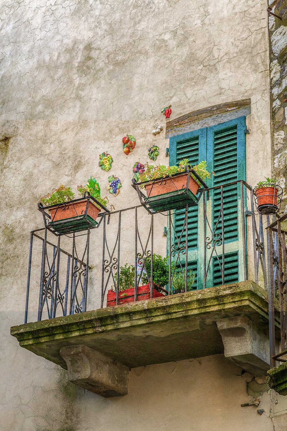 Tuscan balcony with green shutters, terracotta pots and aged stone walls.