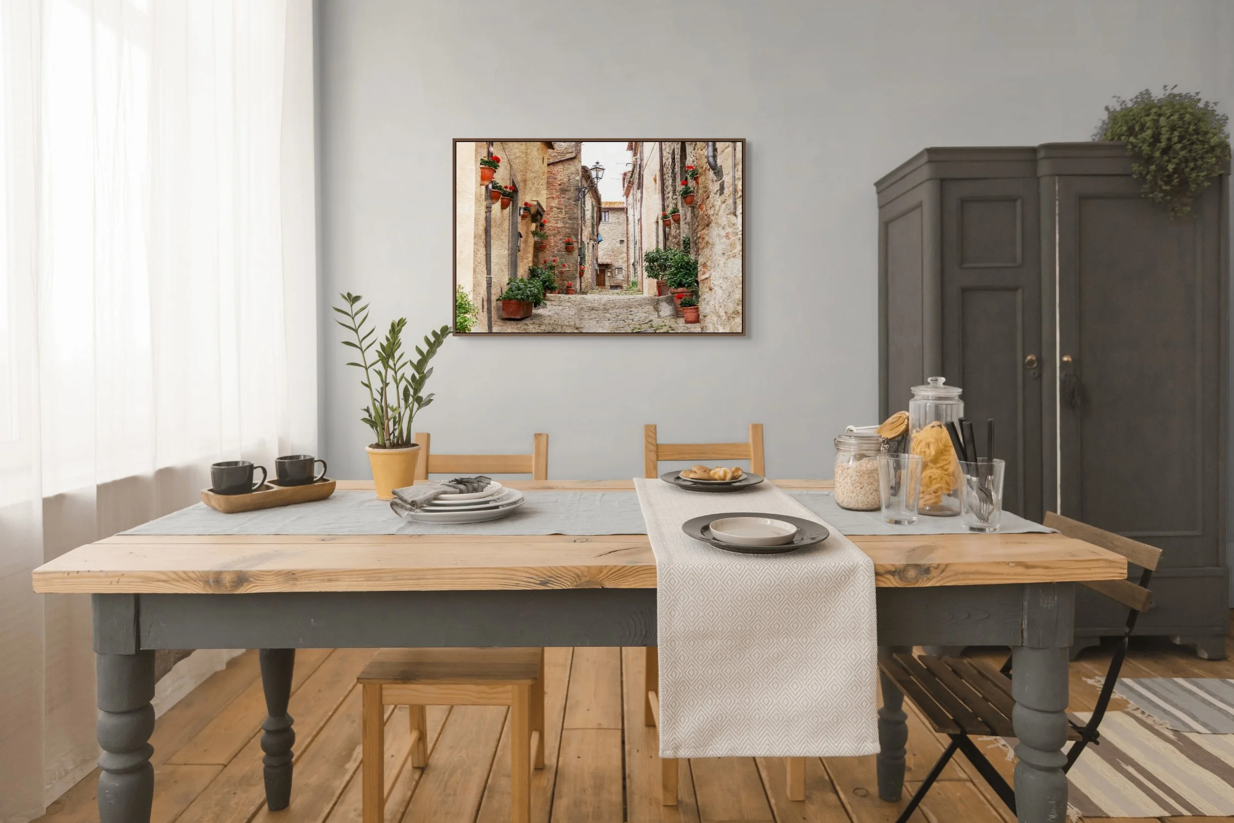 Cobbled street in an Italian village lined with terracotta pots and red geraniums.